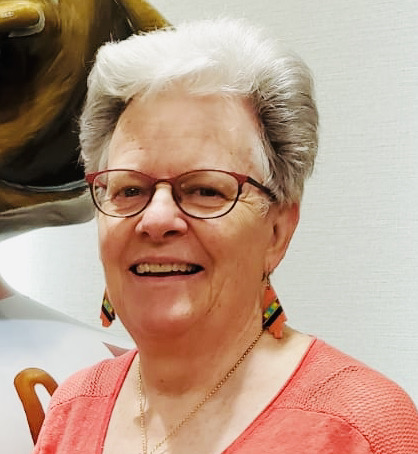 Claire Cassidy is an older woman with short white hair. She is wearing maroon glasses and pretty earrings with an orange/salmon sweater.